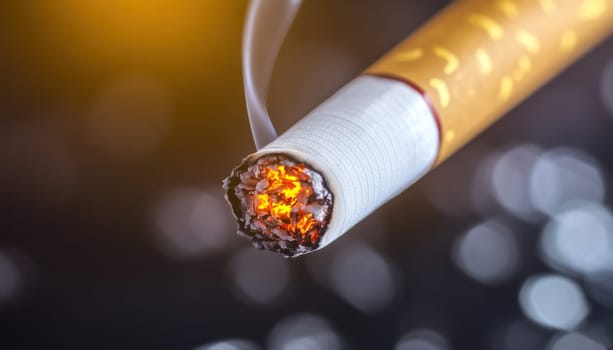 Close up of a lit cigarette emitting smoke, highlighting the dangers of smoking and tobacco addiction