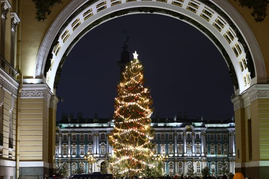 A beautifully lit and adorned Christmas tree stands majestically and gracefully beneath a grand arch at night