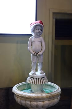 A charming and cute boy statue elegantly standing in a beautiful fountain, adorned with a cheerful holiday hat