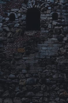 Close-up of an ancient stone and brick wall featuring a dark arched window, weathered texture, and intricate masonry.