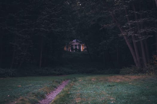 A narrow path leading to a yellow villa surrounded by dense forest trees, captured at twilight.