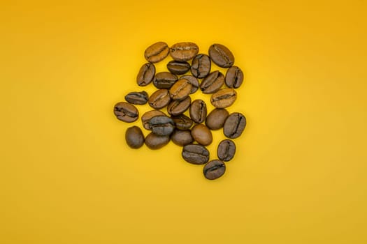 Minimalist arrangement of roasted coffee beans scattered on a vibrant yellow background, highlighting their rich texture and brown tones.