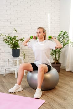 Woman exercising with dumbbells on a stability ball in a bright indoor space