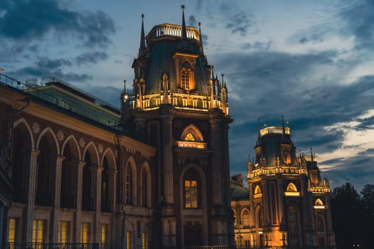 Gothic-style palace with illuminated towers and arched windows, set against a dramatic evening sky, showcasing intricate architectural details.