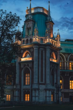 Close-up of a Gothic-style tower with arched windows and spires, warmly illuminated at dusk under a twilight sky.