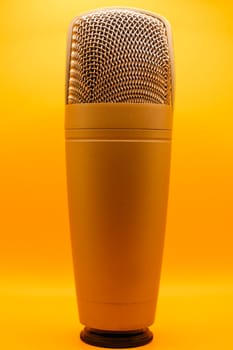 Close-up of a professional gold studio microphone isolated against a bright orange background.