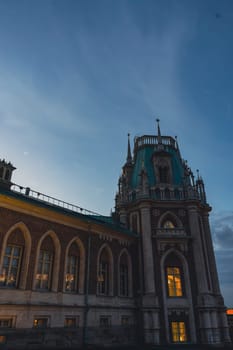 Close-up of a Gothic-style palace tower with spires and illuminated arched windows, captured under a serene twilight sky.