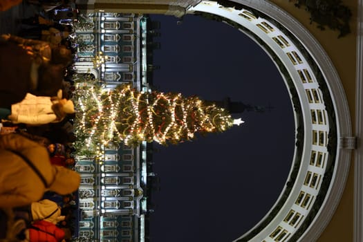A decorated Christmas tree radiates warmth, lighting up the winter night, surrounded by joyful visitors and cheer