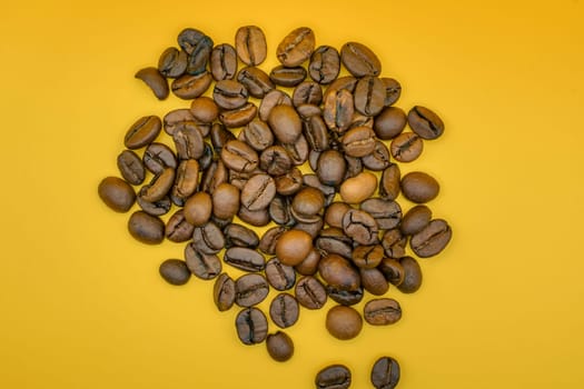 Overhead view of a heap of roasted coffee beans spread on a vibrant yellow background, showcasing their rich color and texture.