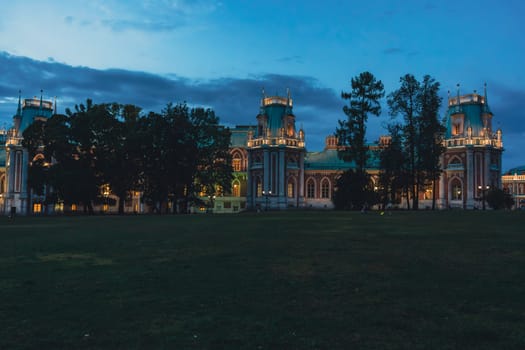 A panoramic view of a Gothic-style palace with glowing windows and illuminated towers, surrounded by trees, captured under a twilight sky.