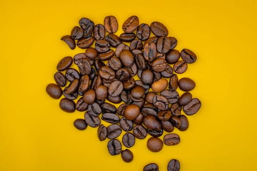 Overhead view of roasted coffee beans scattered on a bright yellow background, showcasing their rich brown tones and texture.