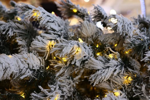 A detailed closeup view of snowy pine branches beautifully adorned with warm, glowing lights for the holiday season