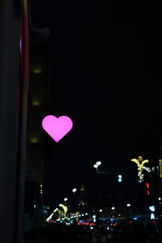 A vibrant urban night scene features a heartshaped light, symbolizing love amidst the lively city life