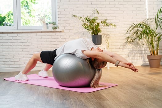 Young woman exercising on a stability ball in a bright room with plants close up