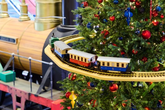A colorful train gracefully circles around a beautifully decorated Christmas tree, bringing joy and cheer