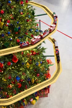 A vibrant Christmas tree is adorned with colorful ornaments and has a train track winding around its branches