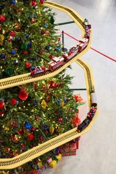 A beautifully vibrant Christmas tree is adorned with colorful ornaments and surrounded by a toy train track