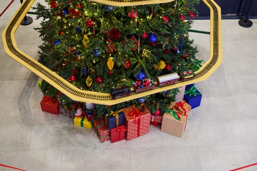 A beautifully decorated Christmas tree stands surrounded by colorful gifts and a festive train track