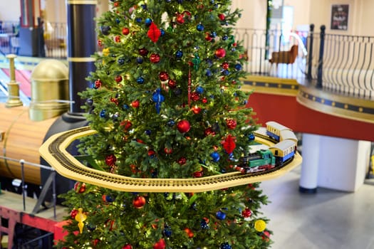 A beautifully vibrant Christmas tree adorned with colorful ornaments and a delightful model train track