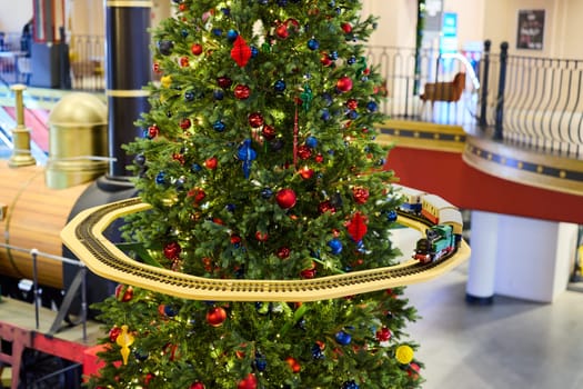 A vibrant and beautifully decorated Christmas tree is adorned with colorful ornaments, including a charming train track