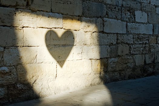 A shadow of a heart is cast on a wall. The heart is in the center of the shadow and is surrounded by the wall