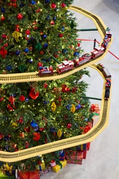 A festive Christmas tree is adorned with colorful ornaments and a charming train set running around it