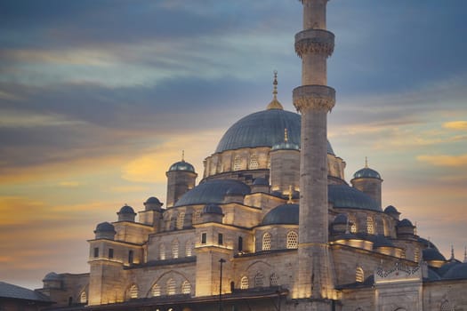 A beautifully lit mosque stands majestically under a vibrant sunset sky filled with colors
