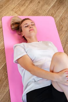 Woman doing floor exercises on a pink mat in a bright, plant-filled room