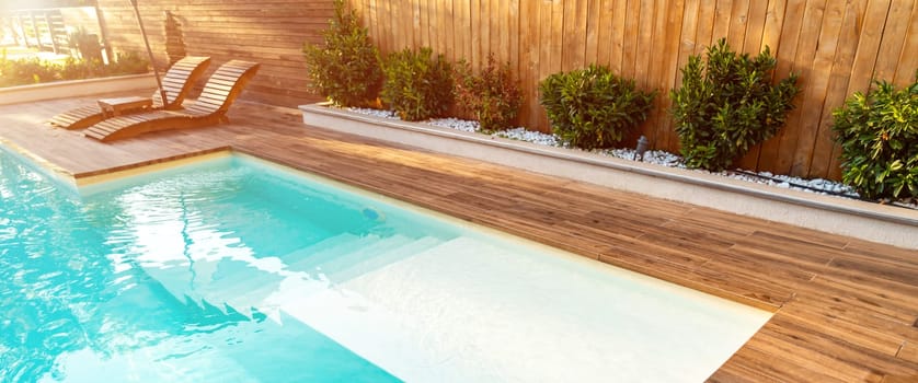 Bright and inviting swimming pool with wooden deck, cozy sun loungers, and lush greenery creating a serene outdoor retreat