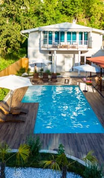 Modern backyard with swimming pool, wooden deck, and lush greenery surrounding a stylish two-story house