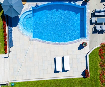 Aerial view of a luxury curved pool with surrounding patio, lounge chairs, and vibrant landscaping