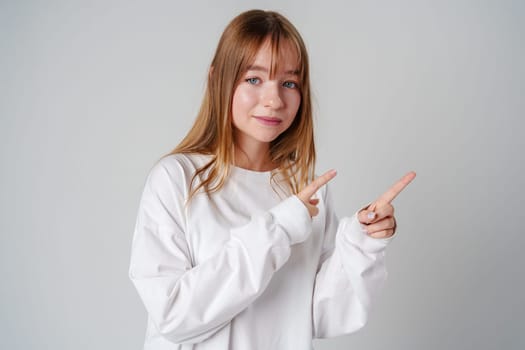 Young girl happily pointing against a neutral background while wearing a cozy white sweatshirt close up