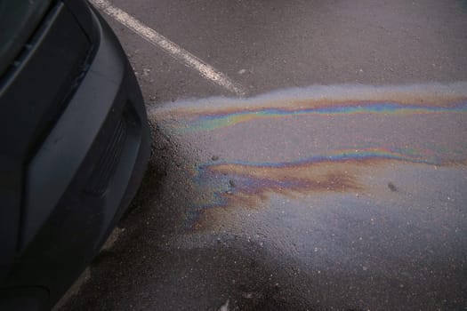 Colorful gasoline or oil spill creating a rainbow sheen on wet asphalt near a car bumper, highlighting environmental pollution.