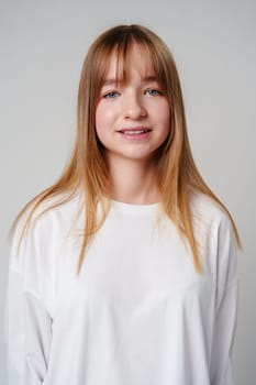 Young woman with long hair in a white sweatshirt standing against a light gray background close up