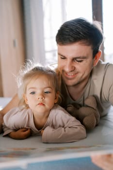 Dad reading a book to a little girl lying on his stomach on the bed. High quality photo