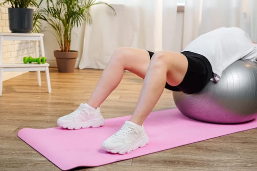 Young woman exercising on a stability ball in a bright room with plants close up