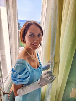 A young lady dressed in a vintage gown stands by the window in an ancient castle, capturing a moment of elegance and nostalgia.
