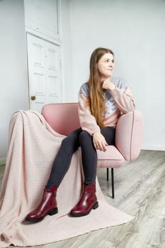 A model poses thoughtfully on a pink couch, showcasing trendy shoes, in a minimalist room with natural light.