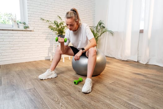 Woman exercising with dumbbells on a stability ball in a bright indoor space