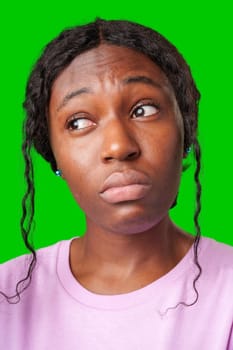 Young woman with curly hair shows a skeptical expression against a bright green background in studio