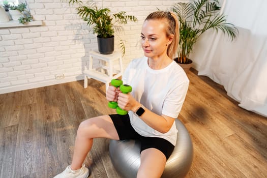 Woman exercising with dumbbells on a stability ball in a bright indoor space