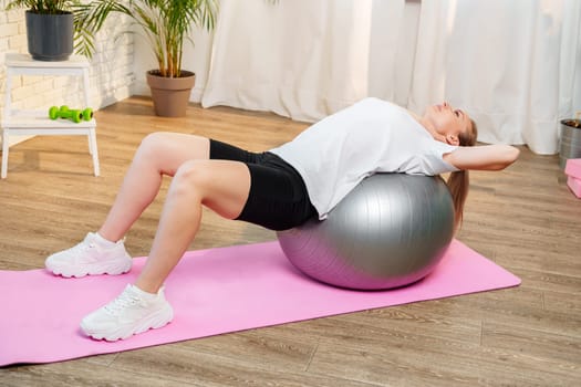 Young woman exercising on a stability ball in a bright room with plants close up