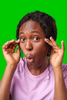 Surprised woman expressing shock while posing with hands on her face against a bright green backdrop close up