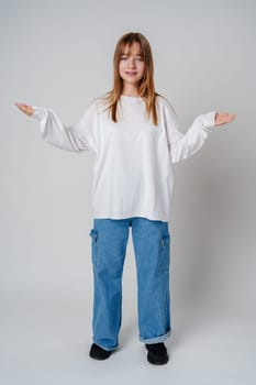 A young girl wearing a white long-sleeve shirt expressing confusion in a minimalistic gray studio setting close up