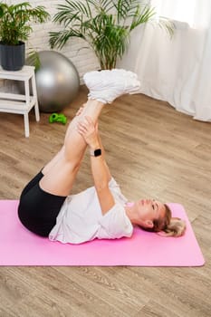 Woman doing floor exercises on a pink mat in a bright, plant-filled room