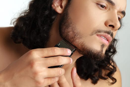 Man trimming his beard indoors using an electric trimmer while showcasing his personal grooming routine close up