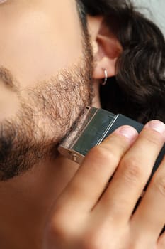 Man trimming his beard indoors using an electric trimmer while showcasing his personal grooming routine close up