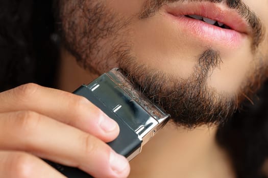 Man trimming his beard indoors using an electric trimmer while showcasing his personal grooming routine close up