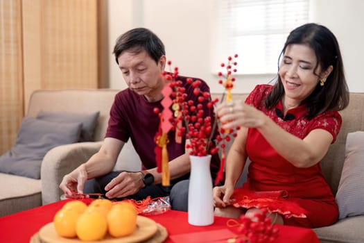 An elderly couple joyfully prepares for Chinese New Year creating vibrant decorations together in their comfortable home.