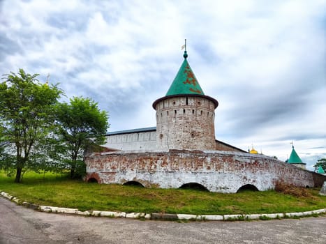 Kremlin in Yaroslavl features distinctive towers and walls surrounded by vibrant greenery under a cloudy sky.